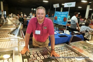 man behind a table of coins at a show
